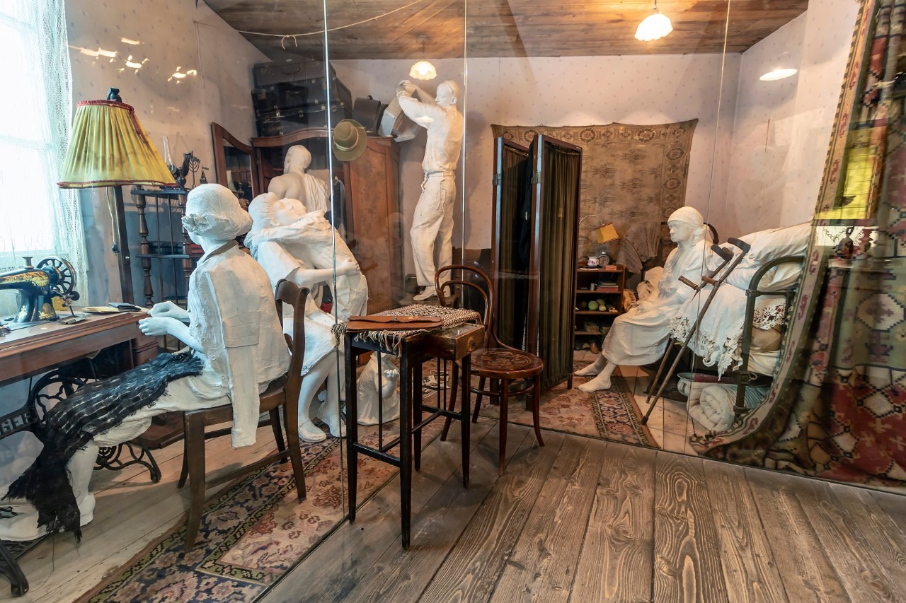 Several life-size figures can be seen behind glass performing various activities inside the museum. The figures show people both young and old who are completely white like statues © Alfredo/stock.adobe.com