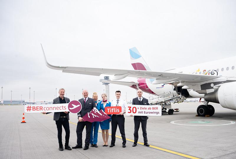 Flugzeug Eurowings am BER. Im Vordergrund Personen die Schilder halten anlässlich des Erstfluges nach Tiflis.
