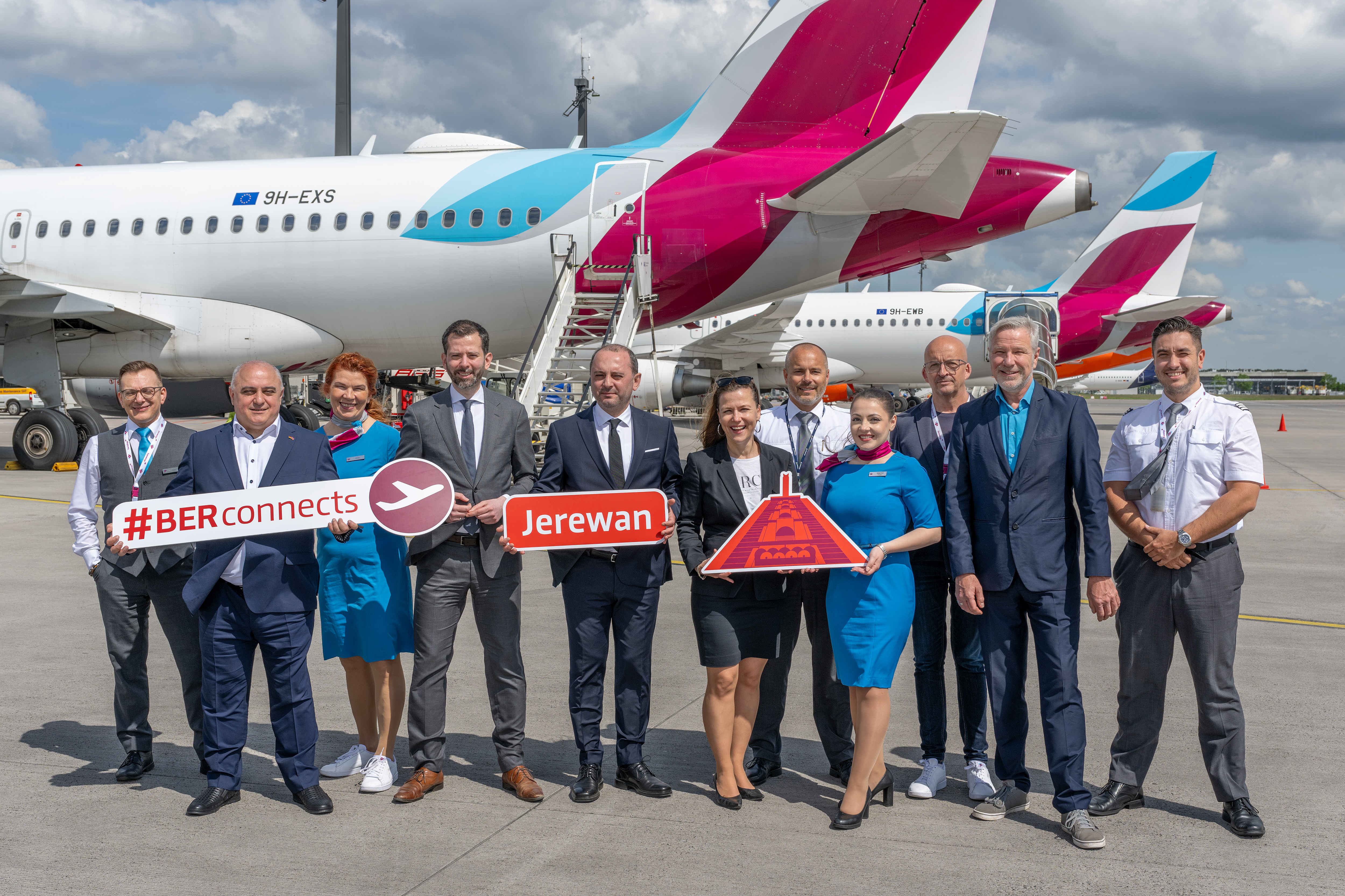 11 people stand in front of a Eurowings aircraft with signs in their hands.