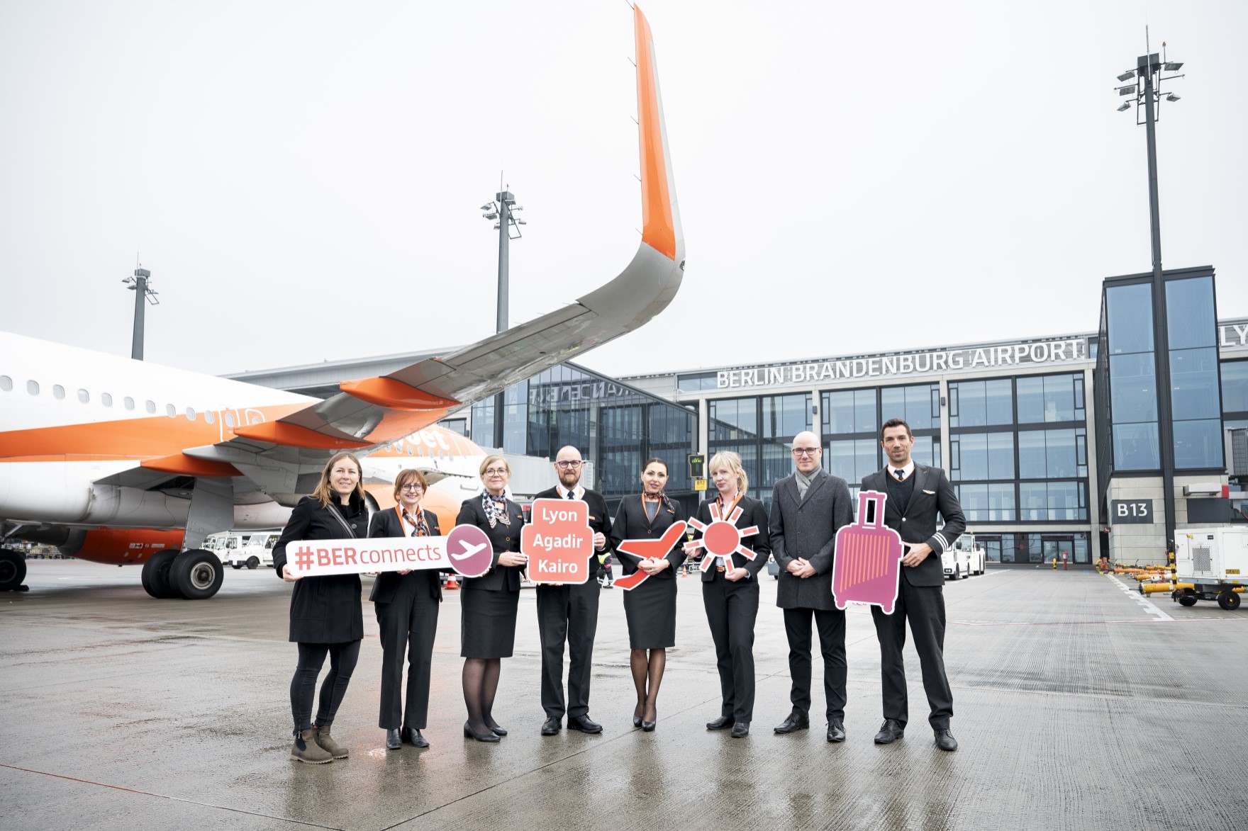 A group of people pose with signs on the apron in front of an aircraft.