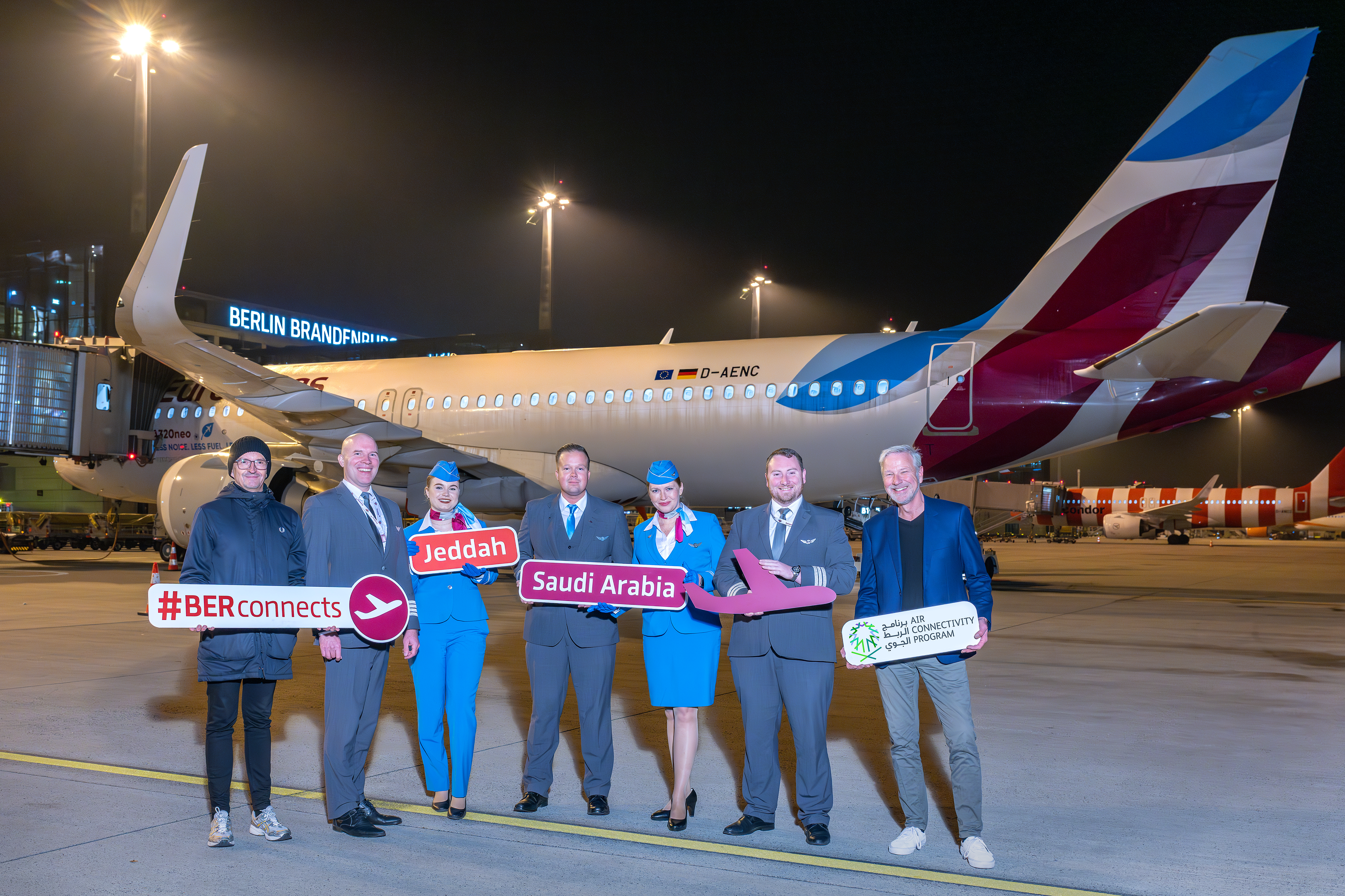 A group of people pose with signs on the apron in front of an aircraft.