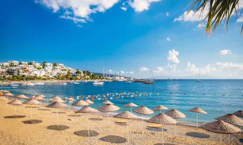 View over a beach with parasols to the sea and the sky, in the background a town can also be seen in the bay