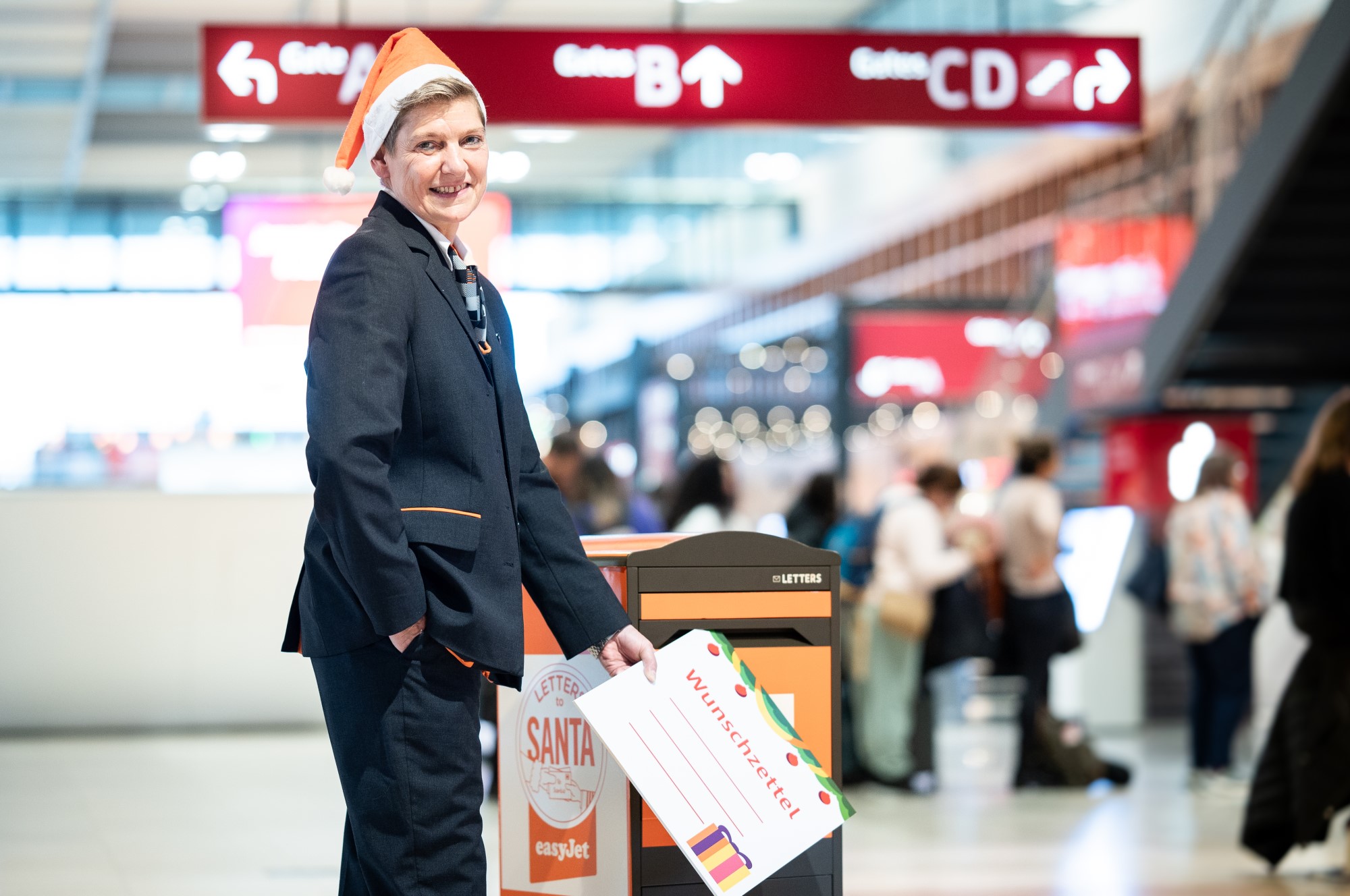 EasyJet Stewardess wirft symbolisch einen Brief an den Weihnachtsmann in einen gebrandeten Briefkasten.