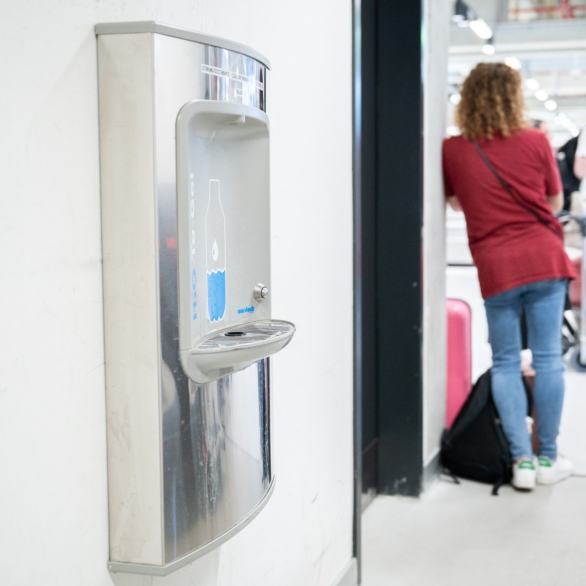 Wasserspender im Terminal 2. Im Hintergrund eine Reisende.