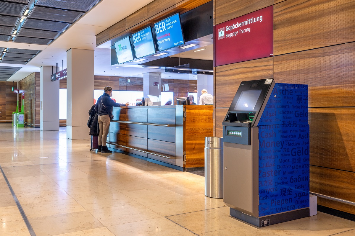 Geldautomat der Berliner Volksbank im BER. Im Hintergrund Menschen an einem Counter.