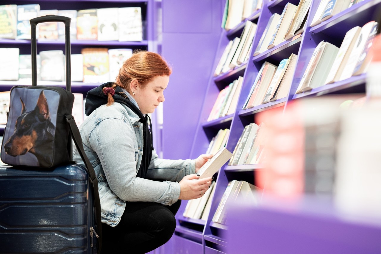 Frau hockt vor einem Regal und liest in einem Buch.