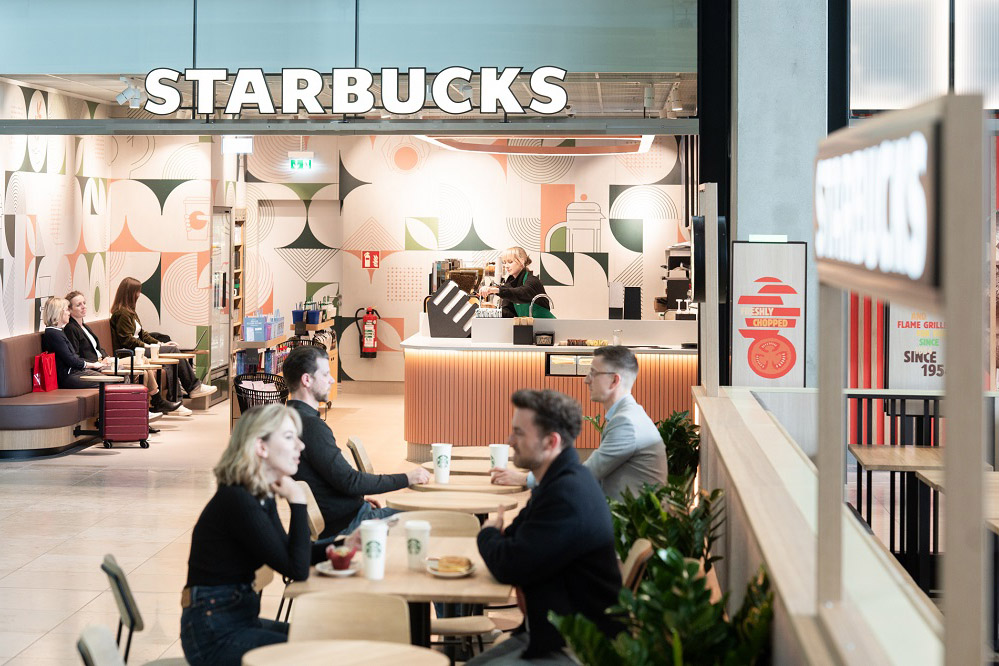Starbucks im Food Court. Menschen sitzen an Tischen. Dahinter das Lokal