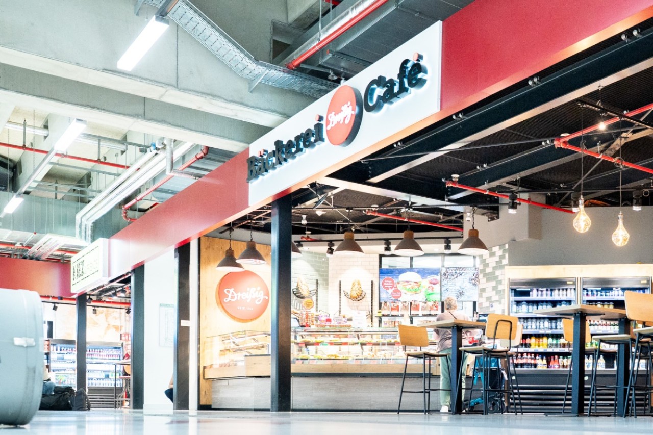 Blick von außen auf das Café Bäckerei Dreißig mit Auslage und Sitzbereich.