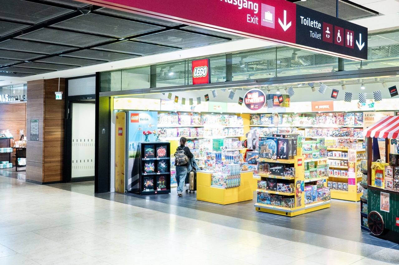 Innenansicht des LEGO Stores im Flughafen Berlin Brandenburg mit bunten LEGO-Sets in Regalen und auf einem Präsentationstisch.