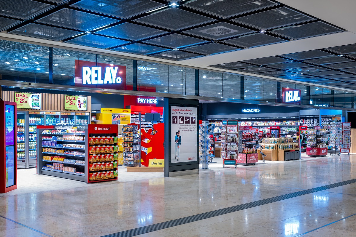 Relay Shop in der Ebene E0 am BER. Zu sehen sind Regale mit Waren und eine gelbe Wand mit Postdienstleistungen