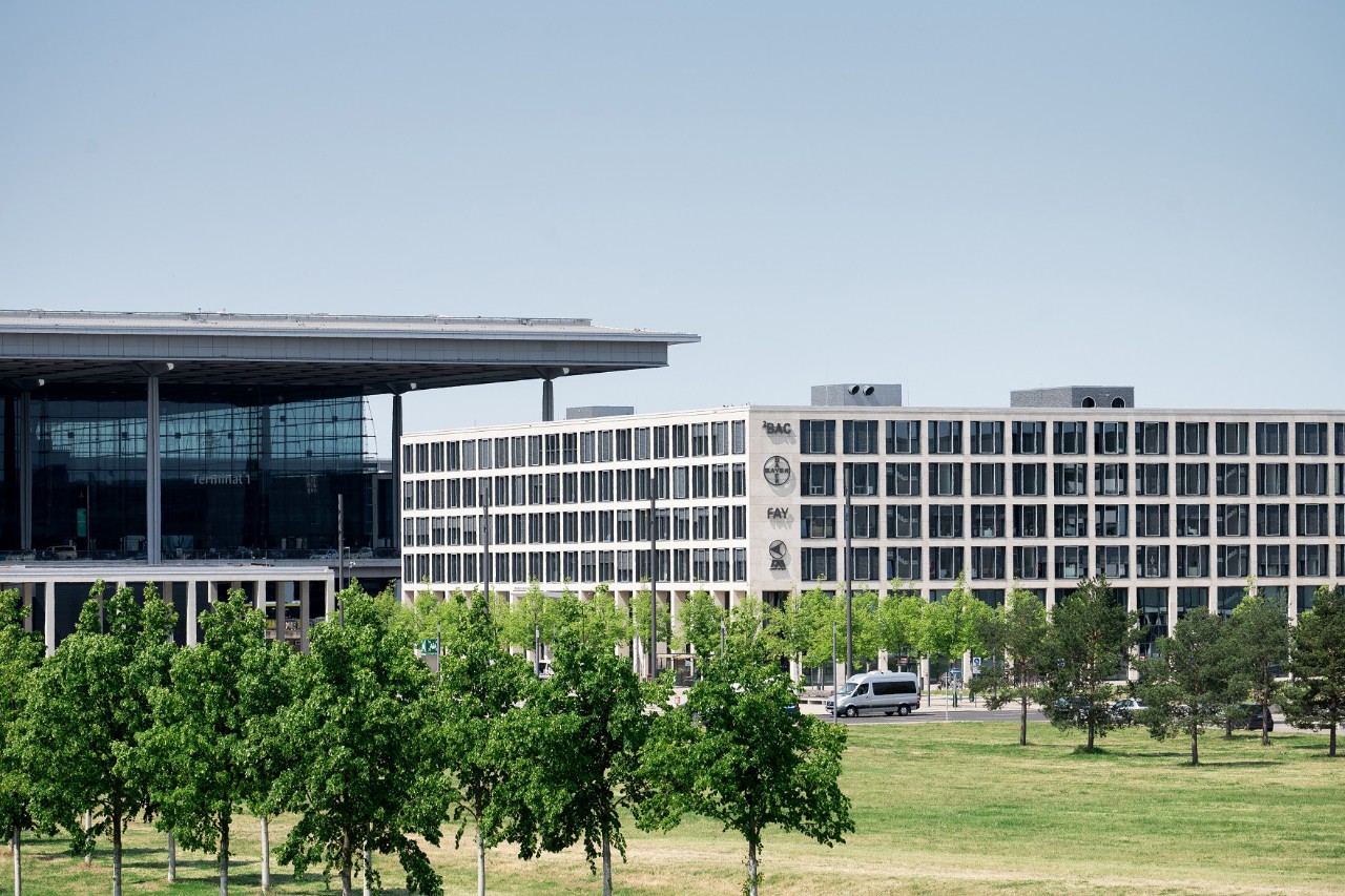 Das Bürogebäude mit dem dahinterliegenden Terminal 1. Davor Bäume und Wiese.
