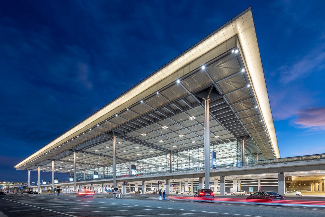 Das beleuchtete Terminal 1 bei Nacht. Davor fahren Autos.
