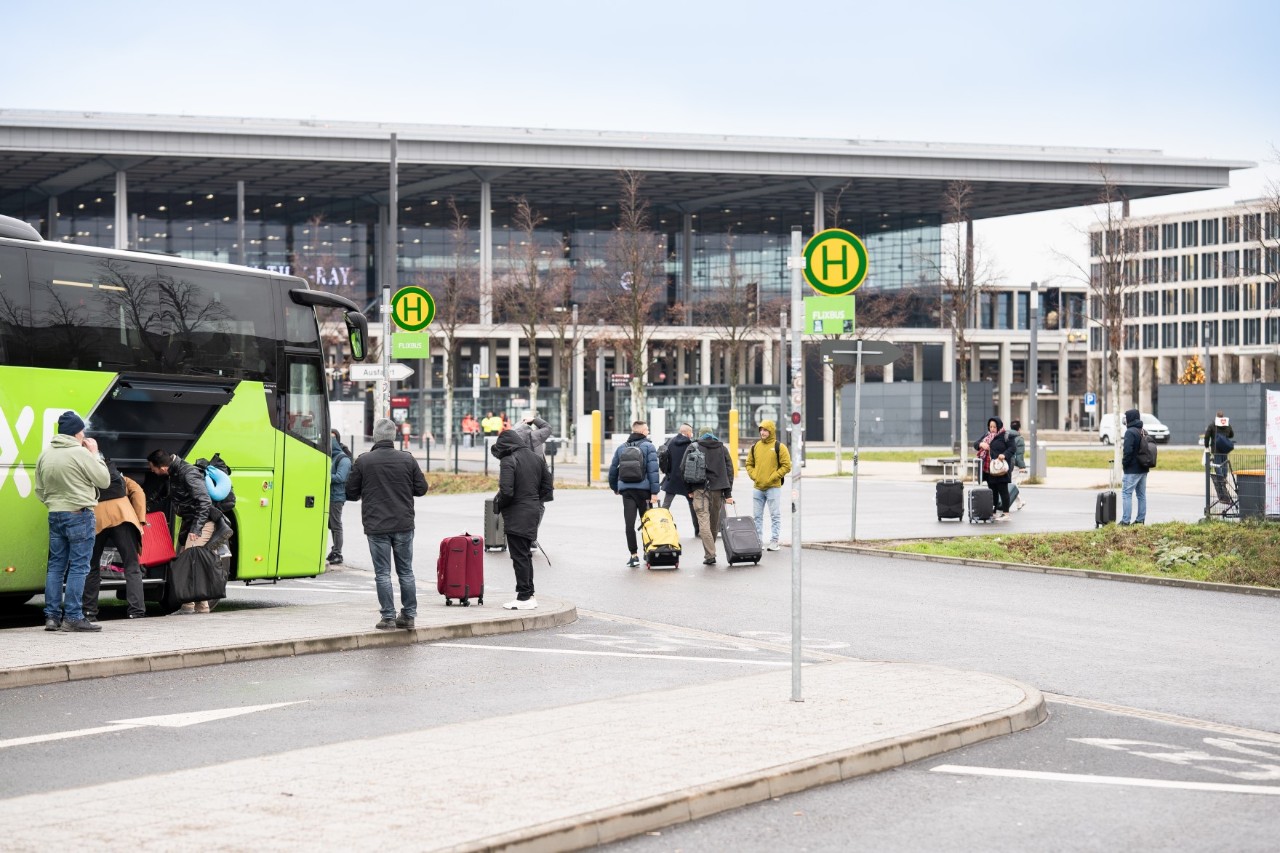 Personen stehen vor einem grünen Bus. Dahinter das Terminal 1.