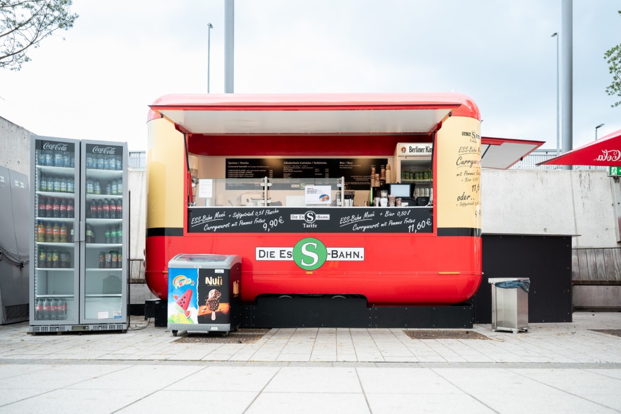 Verkaufswagen, der wie eine S-Bahn aussieht. Daneben ein Getränkeautomat.
