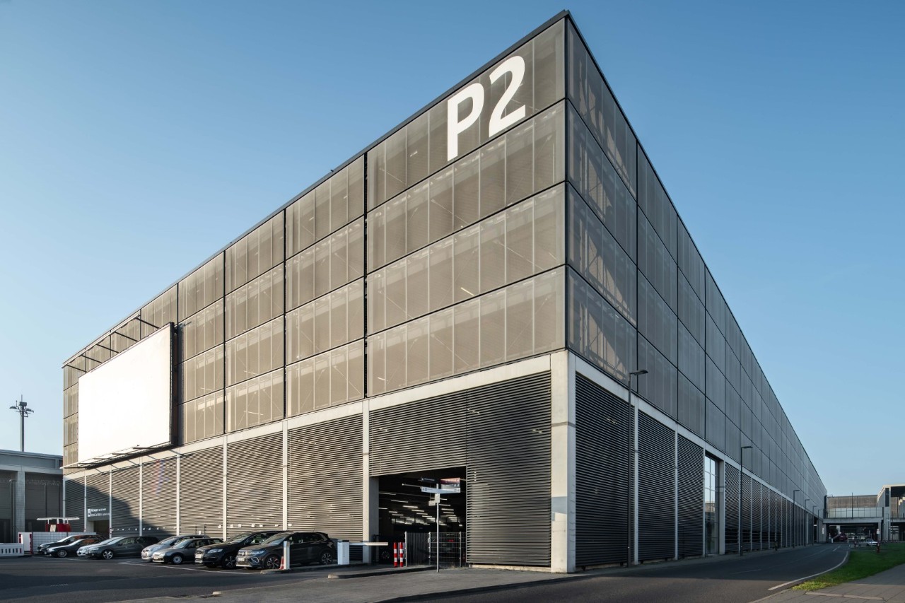 Das graue Parkhaus P2. Davor Autos.