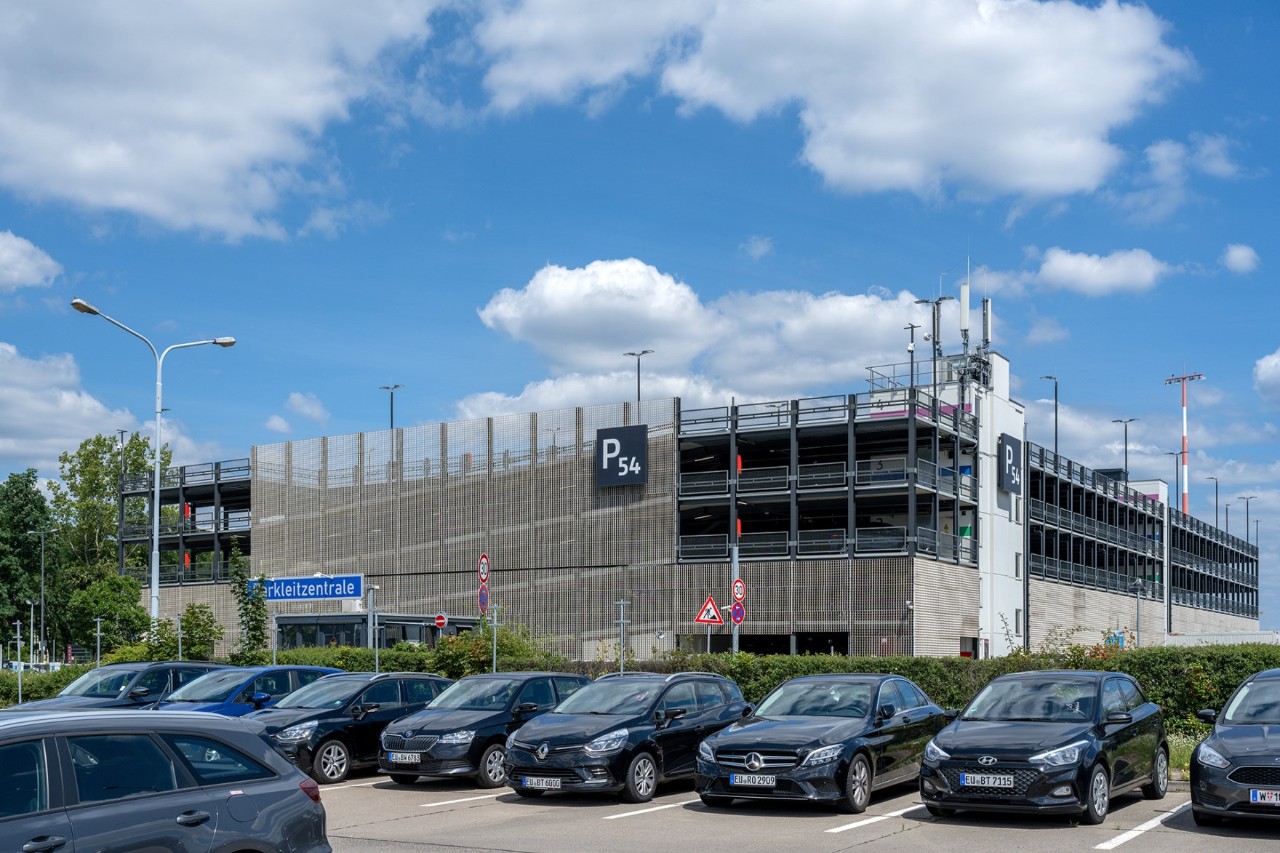 Im Vordergrund viele Autos auf einem Parkplatz. Im Hintergrund das Parkhaus P54.