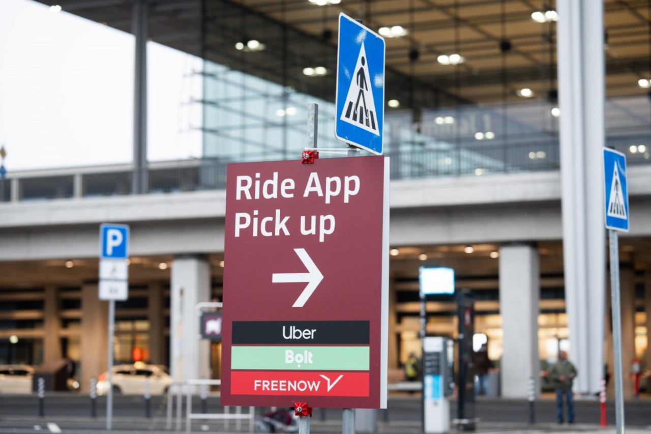 Schild mit dem Aufdruck "Ride App Pick up". Dahinter das Terminal.