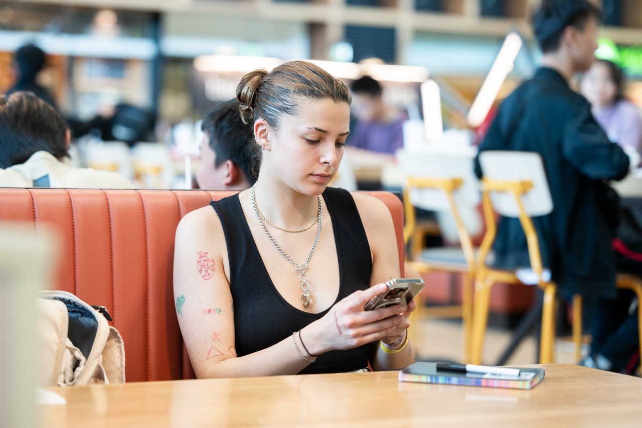 Eine Person schaut auf ein Smartphone und sitzt in einem Café.