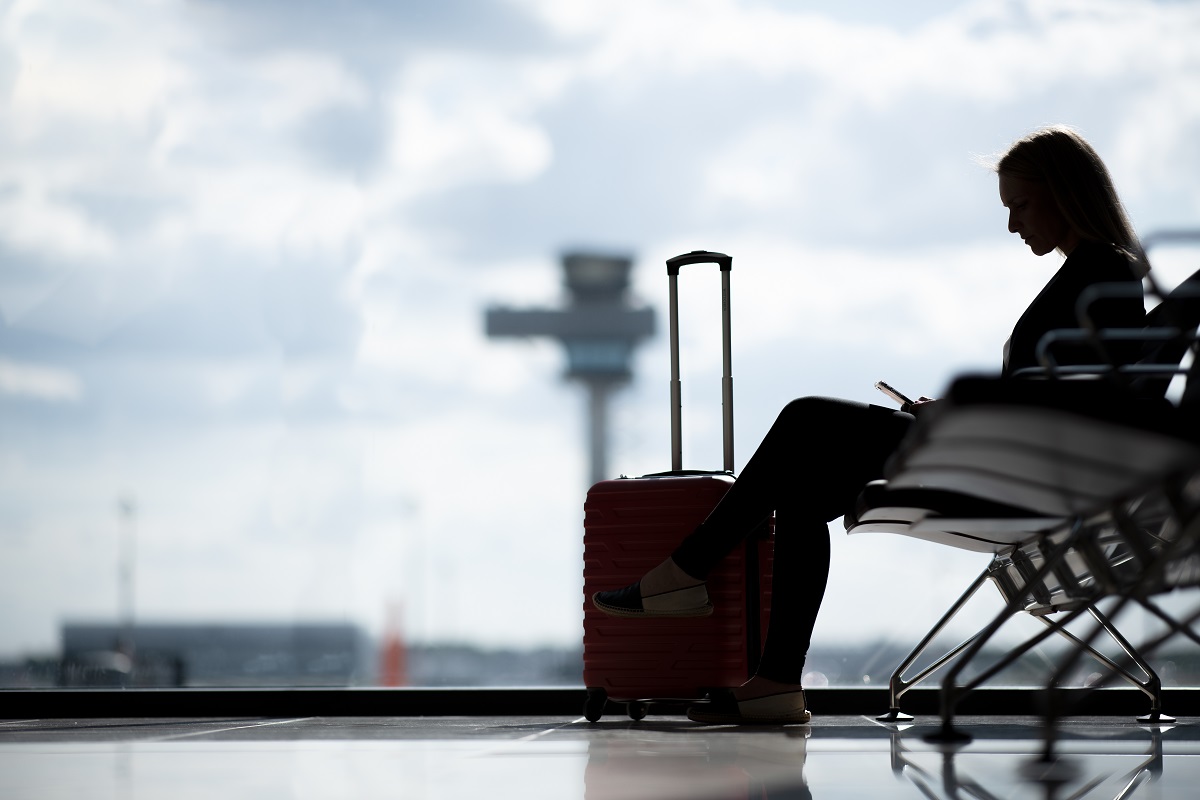 Person sitzt im Gate vor einer Glasscheibe. Dahinter der Tower.