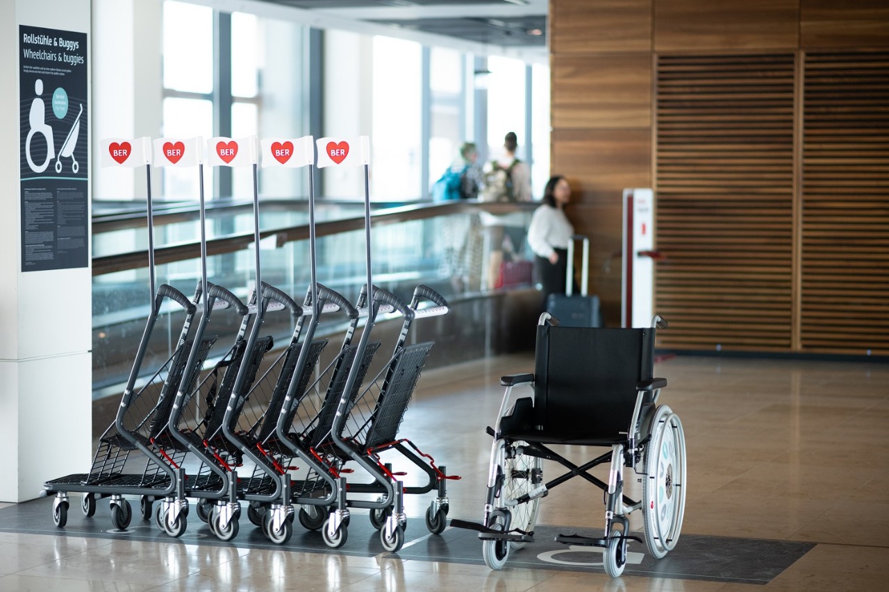 Fünf Kinderbuggies und ein Rollstuhl zur freien Verfügung. Dahinter ein Fahrband.