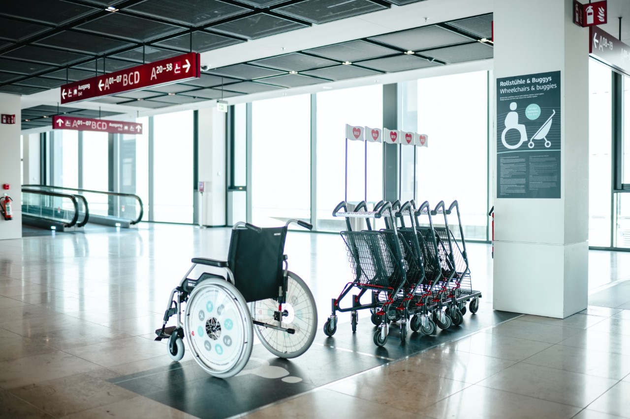 Blick auf zahlreiche Buggys und einen Rollstuhl. Rechts automatische Laufbänder.