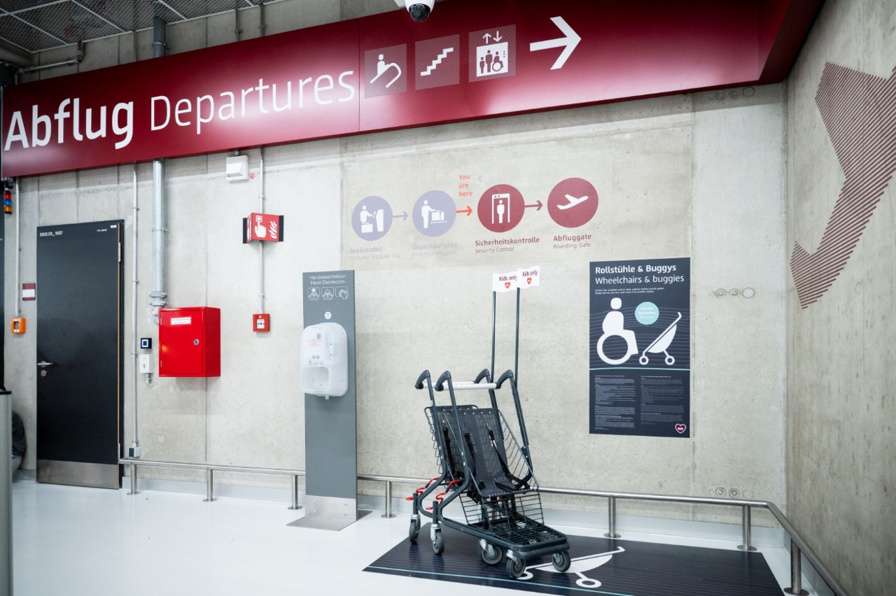 Kinderbuggies zur freien Verfügung vor einer Wand mit Wegeleitung zum Abflug.