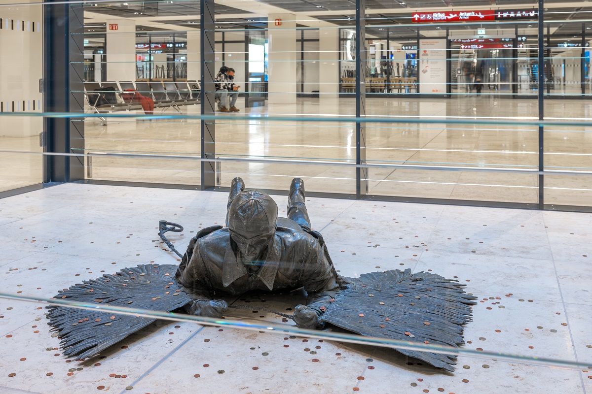 Bronzeskulptur von Rolf Scholz (1985) im Eingangsbereich von Terminal 1 am BER. Sie zeigt einen Piloten in Lederkappe und Flügeln, der auf dem Boden liegt – eine Hommage an Otto Lilienthal und die griechische Sage von Daidalos und Ikaros.