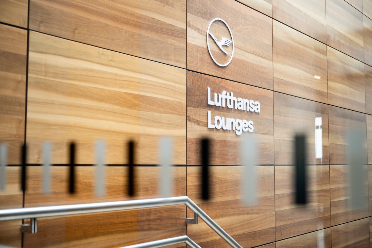 Aufgang zu den Lufthansa Lounges. Lufthansa Logo auf braunem Furnier.