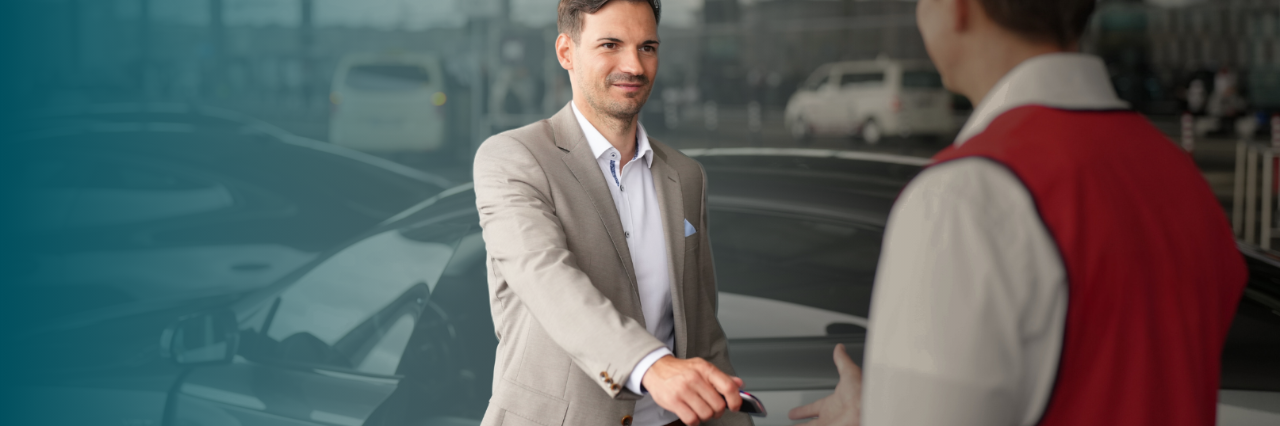 Mann steht vor Auto und übergibt seinen Schlüssel an einen Mitarbeiter des Valet-Parkings.