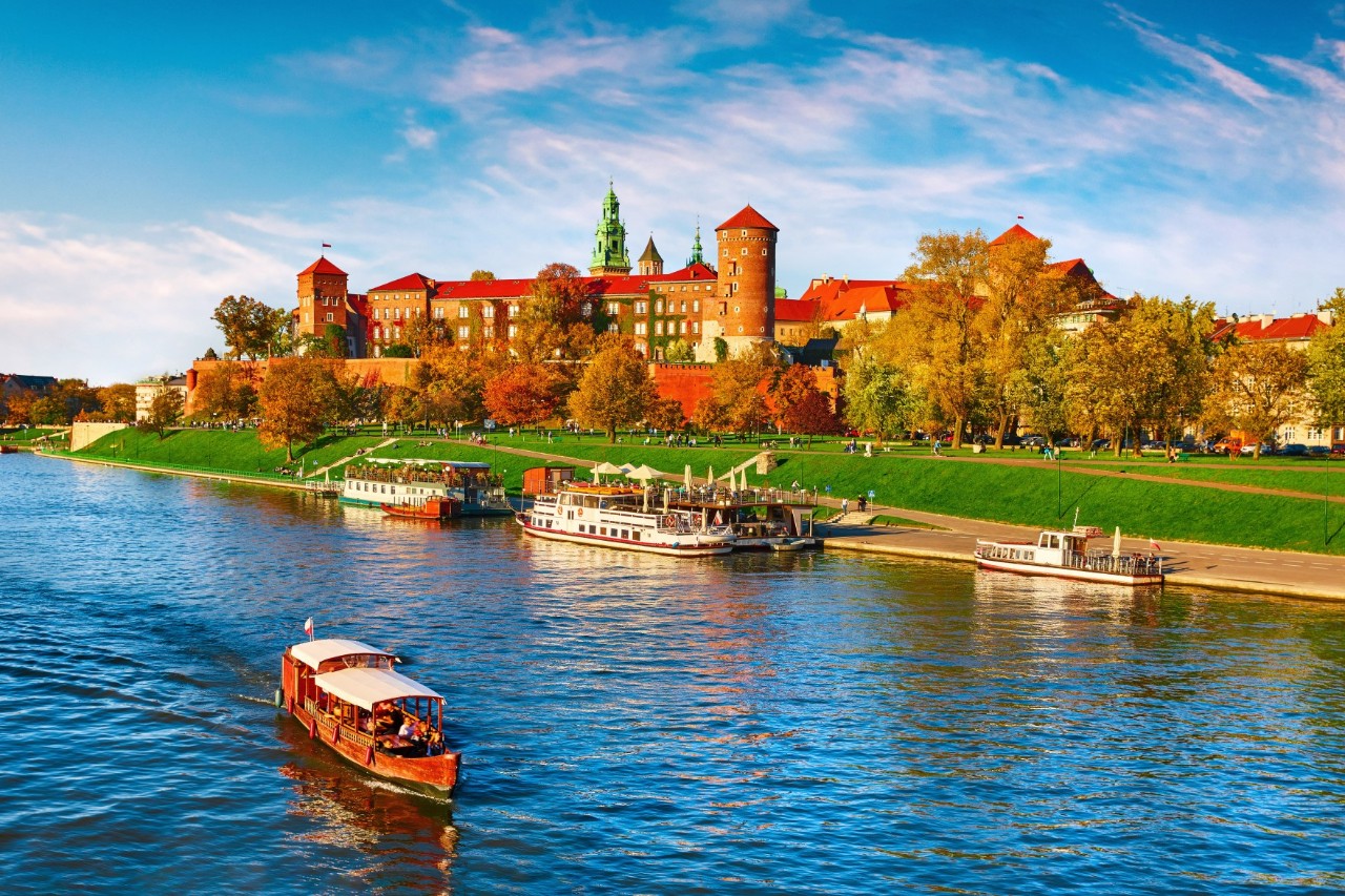 Fluss an dessen Ufer ein Schloss steht Auf dem Fluss fährt ein Ausflugsboot, weitere Boote sind im Hintergrund am Anleger zu sehen 