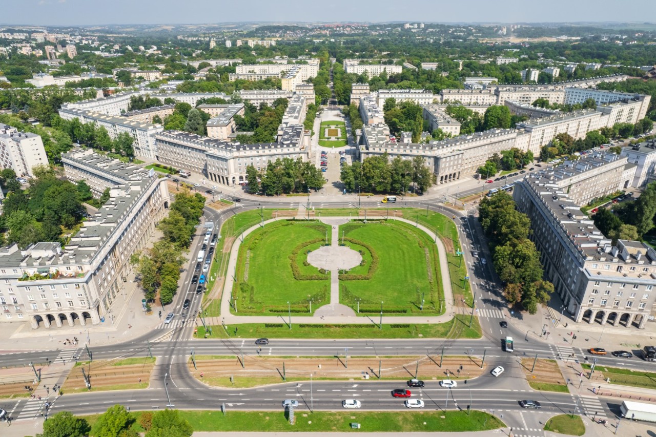 Luftbild auf einen Platz und Parkanlage. Im Vordergrund verläuft eine vierspurige Straße, um den Platz herum befinden sich symmetrisch angeordnet weiße sozialistische Prachtbauten 