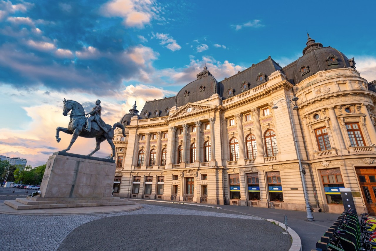 Großes, sandfarbenes Gebäude mit einer Reiterstatue auf dem Platz davor. 