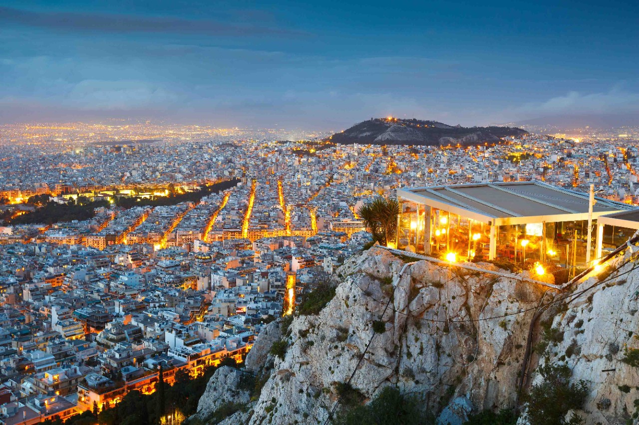 Athen bei Sonnenuntergang mit goldfarbenem Himmel und Stadtsilhouette.