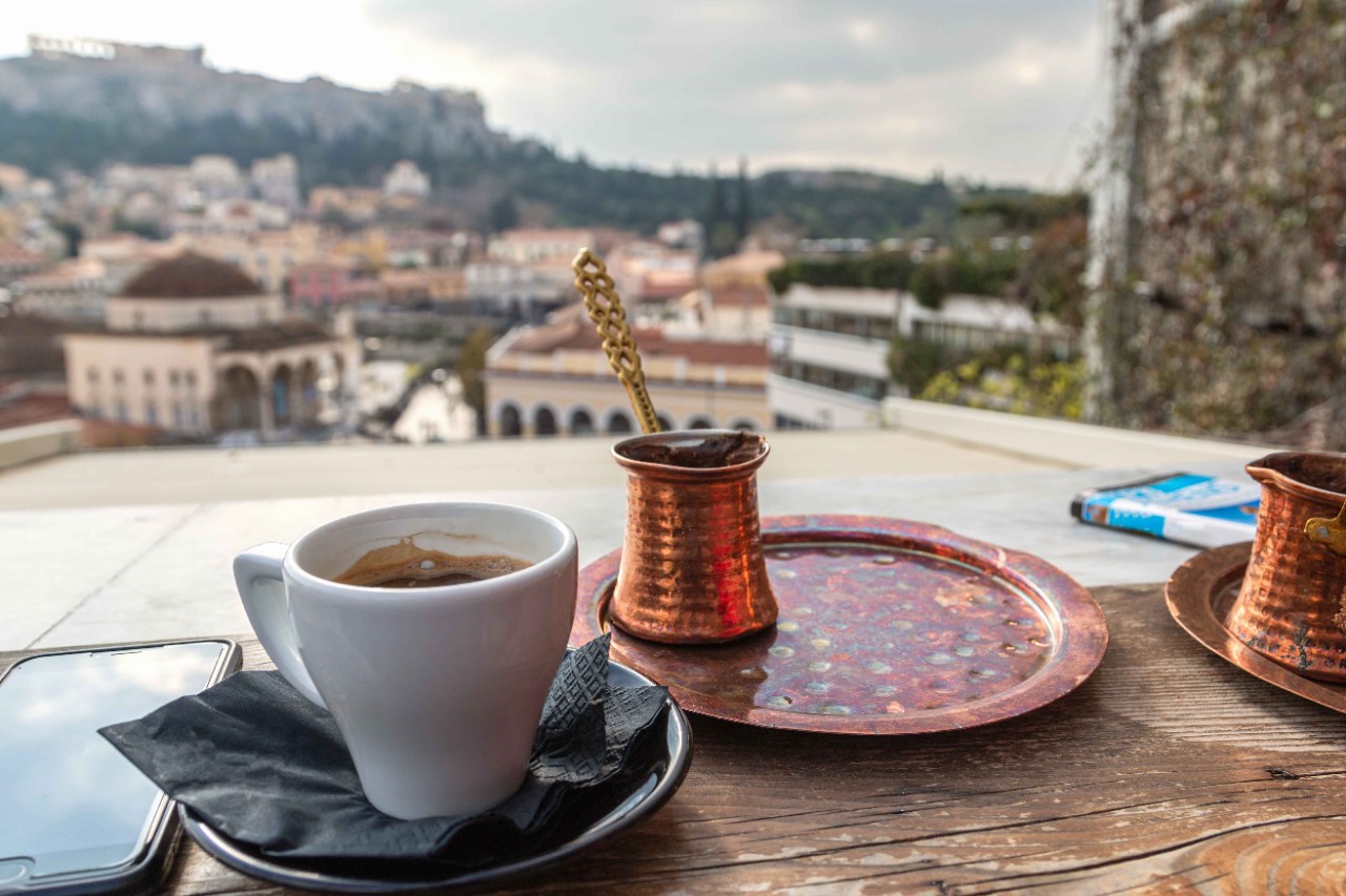 Griechischer Kaffee in kleiner Tasse mit Wasserglas daneben serviert.