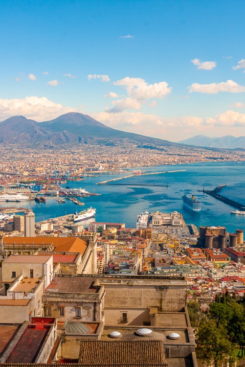 Luftansicht von Neapel, im Vordergrund sind die Altstadt und Häuser, rechts das Meer, am Horizont zeichnet sich der Vesuv ab, Himmel mit Cumulus-Wolken. © pfeifferv/stock.adobe.com