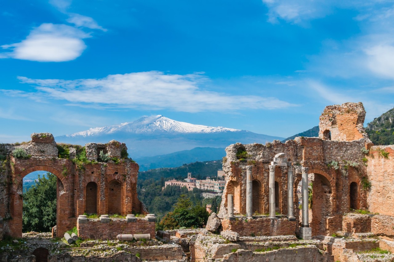 Die Tempelruinen von Taormina. Durch eine Lücke ist der schneebedeckte Vulkan Ätna zu sehen 