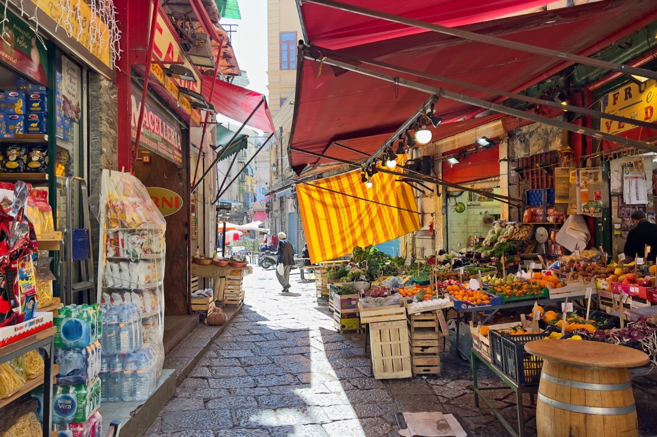 Kopfsteinpflastergasse mit Obst- und Gemüse-Marktständen und Läden 
