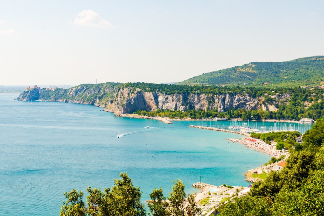 Türkisblaue, weitläufige Bucht mit Steilklippen, grünem Hinterland und Strand mit Booten.