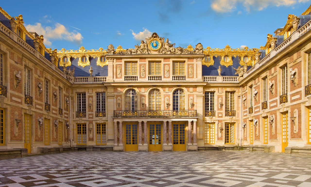 Innenhof von Schloss Versailles mit symmetrischer Fassade und Pflasterung.
