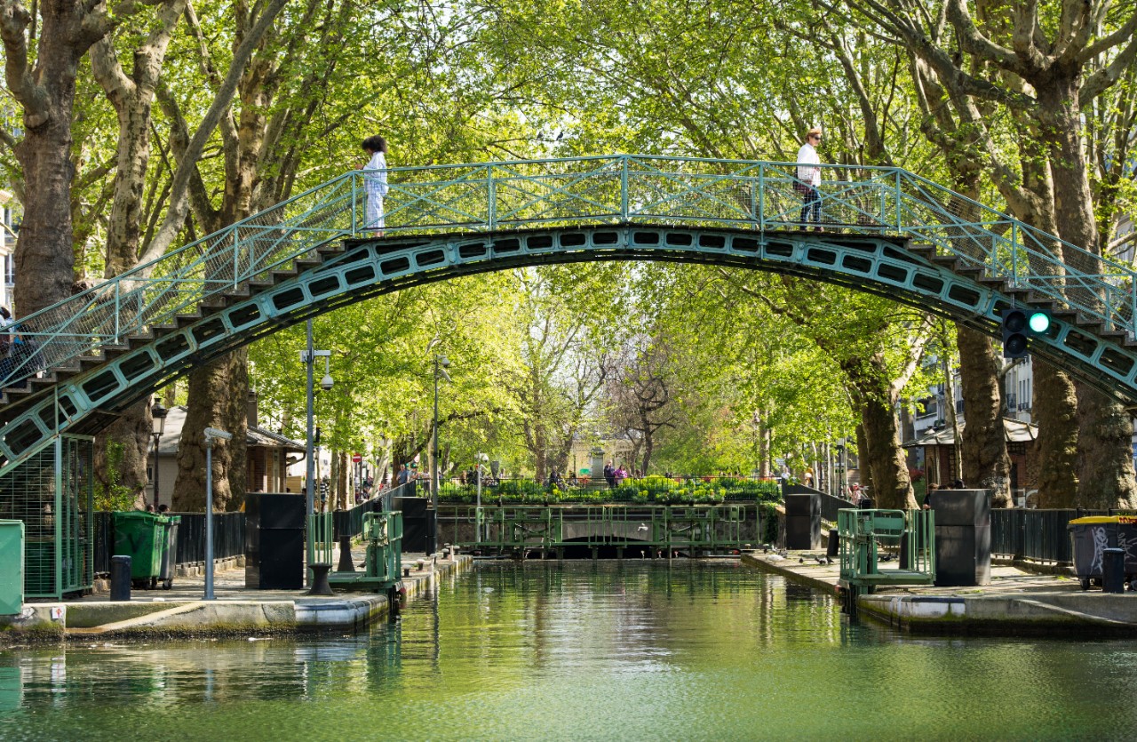  Canal St. Martin mit Uferwegen, Bäumen und Cafés im Pariser Norden.