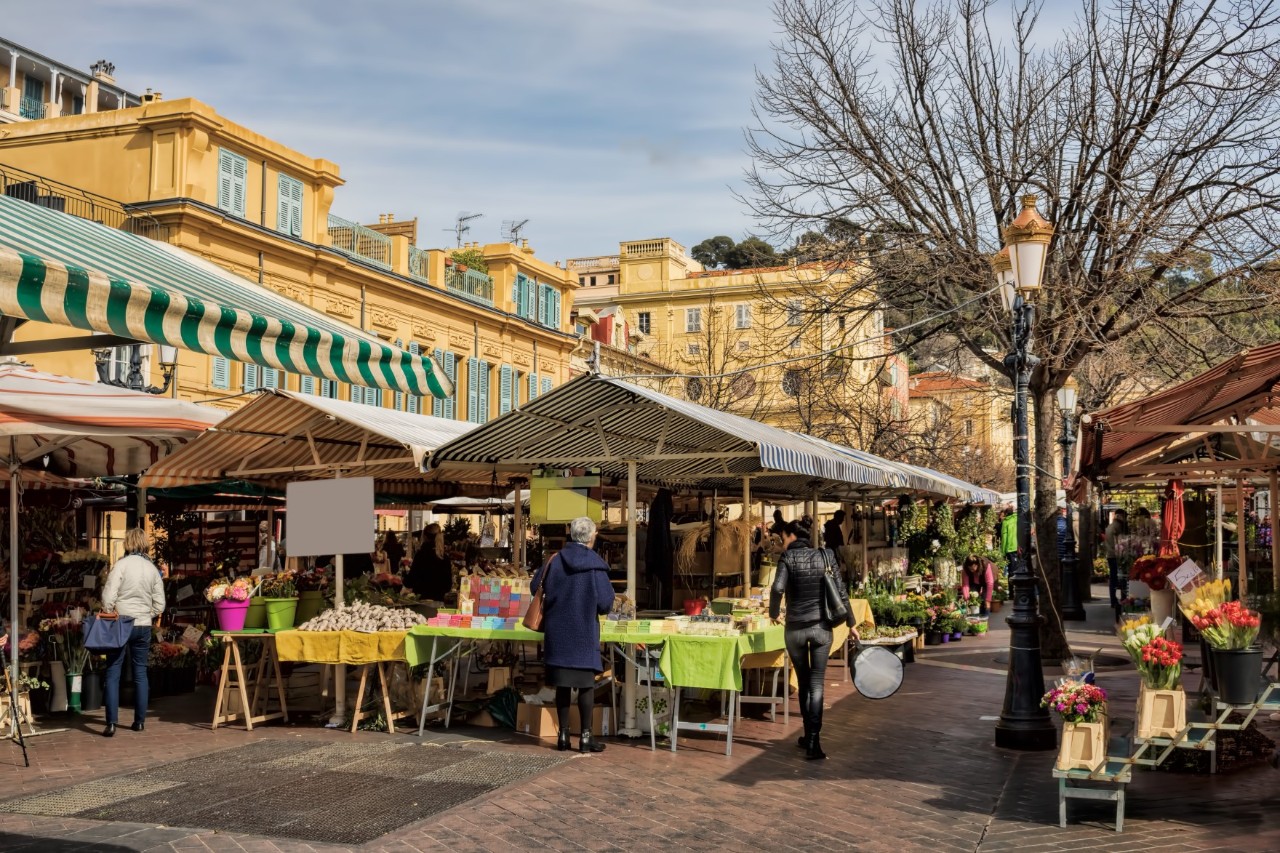 Blumenmarkt Cours Saleya, große Verkaufsstände mit bunt gestreiften Markisen, wenige Menschen, gelbe Häuser hinter dem Markt 