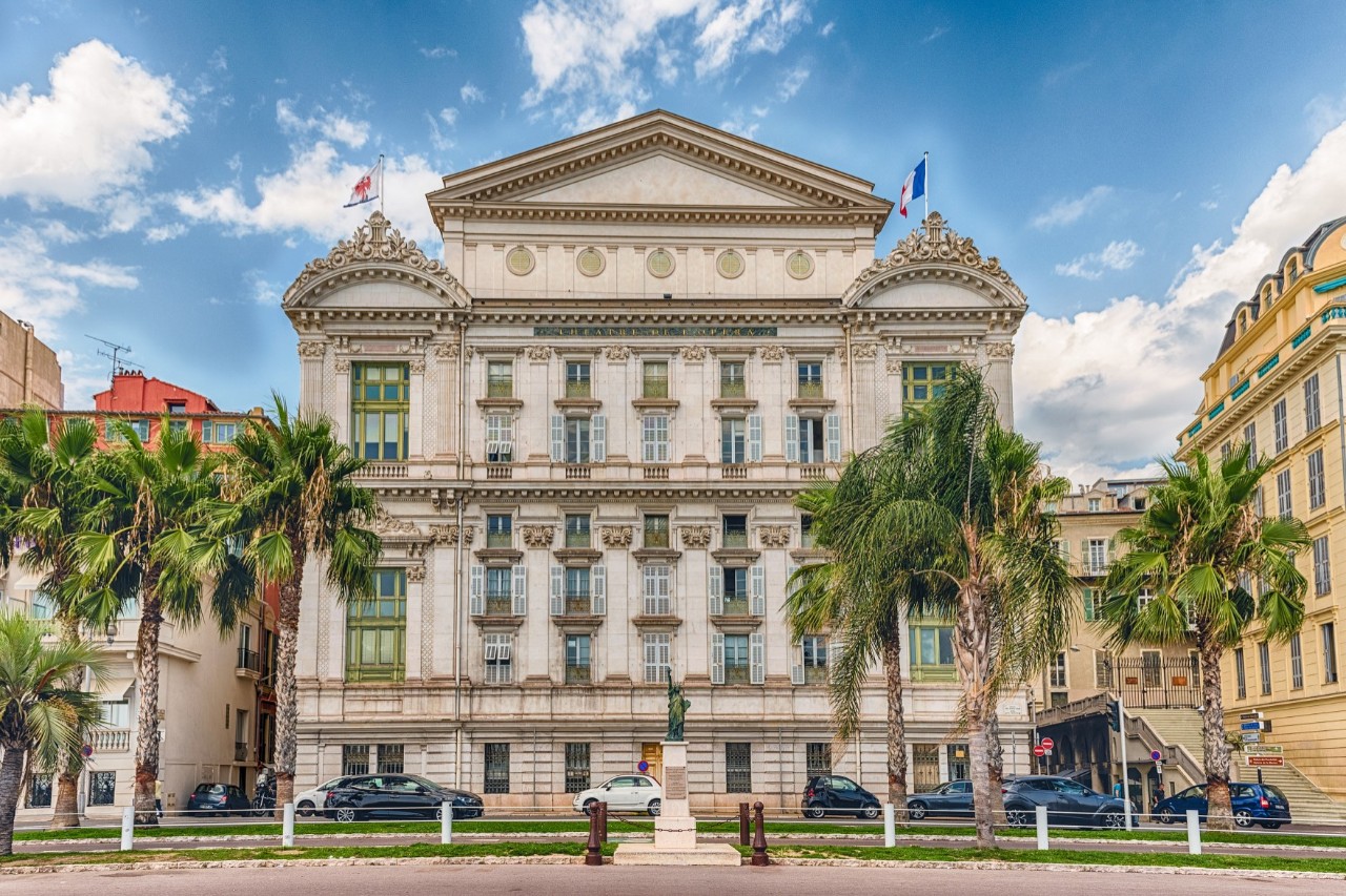 Cremefarbenes Opernhaus im italienischen Stil in Nizzas Altstadt, davor Palmen 