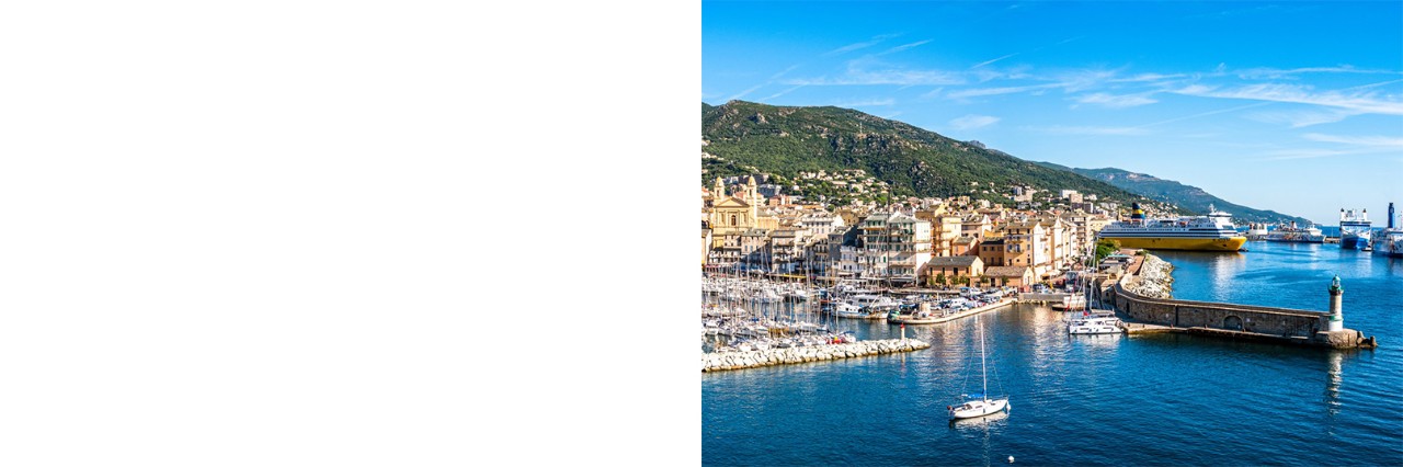 Am Meer gelegene Hafenstadt Bastia mit vielen kleinen Booten, Mole und Leuchtturm sowie grünem, bergigem Hinterland.