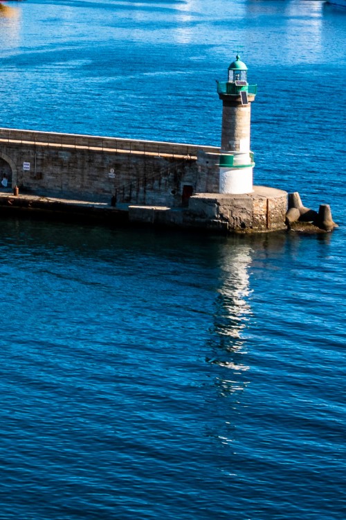 Ein Leuchturm am Ende einer Mole umgeben von dunkelblauem Wasser.