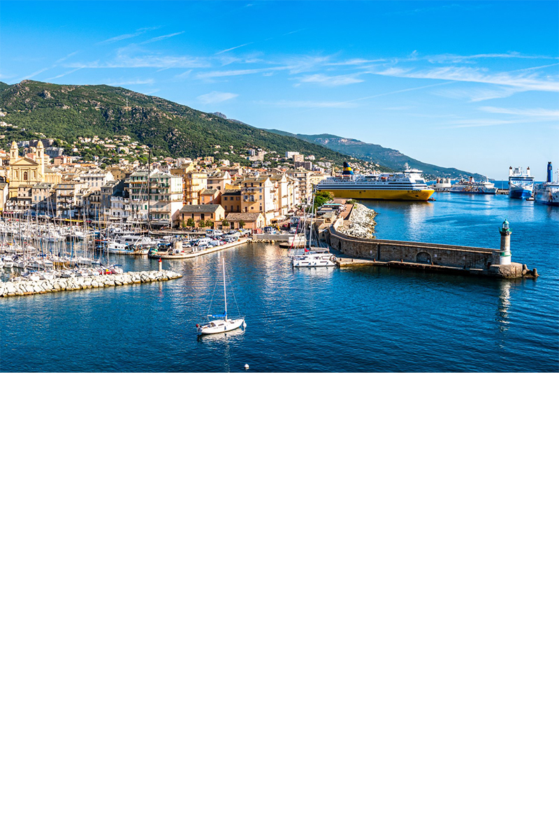 Am Meer gelegene Hafenstadt Bastia mit vielen kleinen Booten, Mole und Leuchtturm sowie grünem, bergigem Hinterland.