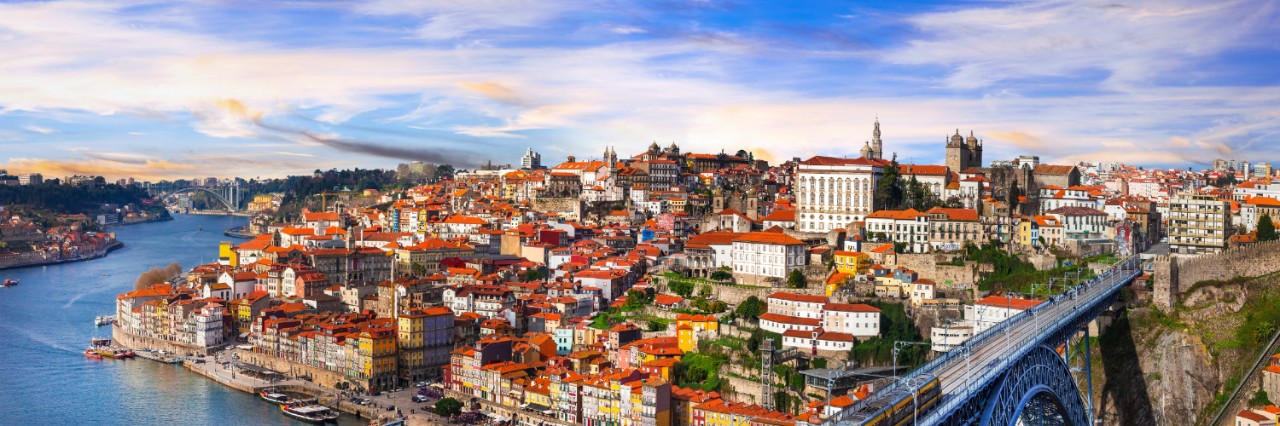Altstadt von Porto auf einem Hügel. Davor ein Fluss mit einer Brücke.