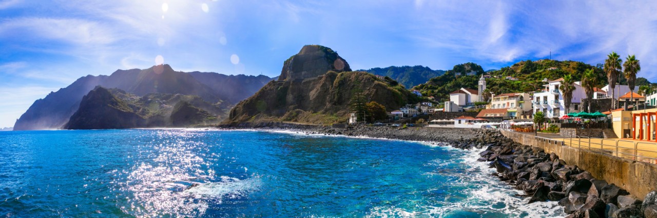 Blick aufs blaue Meer, im Hintergrund felsige Berge, rechts im Bild eine Uferbefestigung und Dorf mit weißen Häusern. © Freesurf/stock.adobe.com  