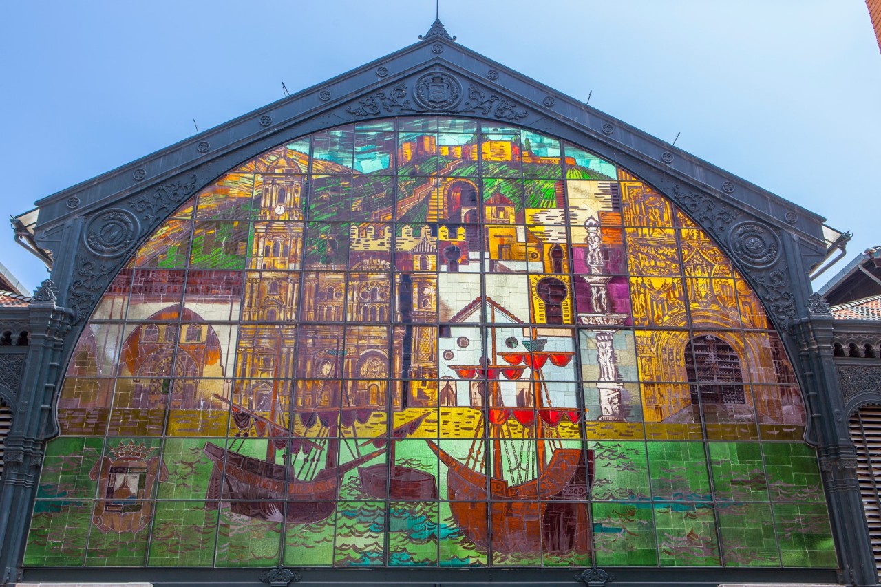 Historische Markthalle mit bunt verglastem Bogenfenster und neugotischer Fassade.