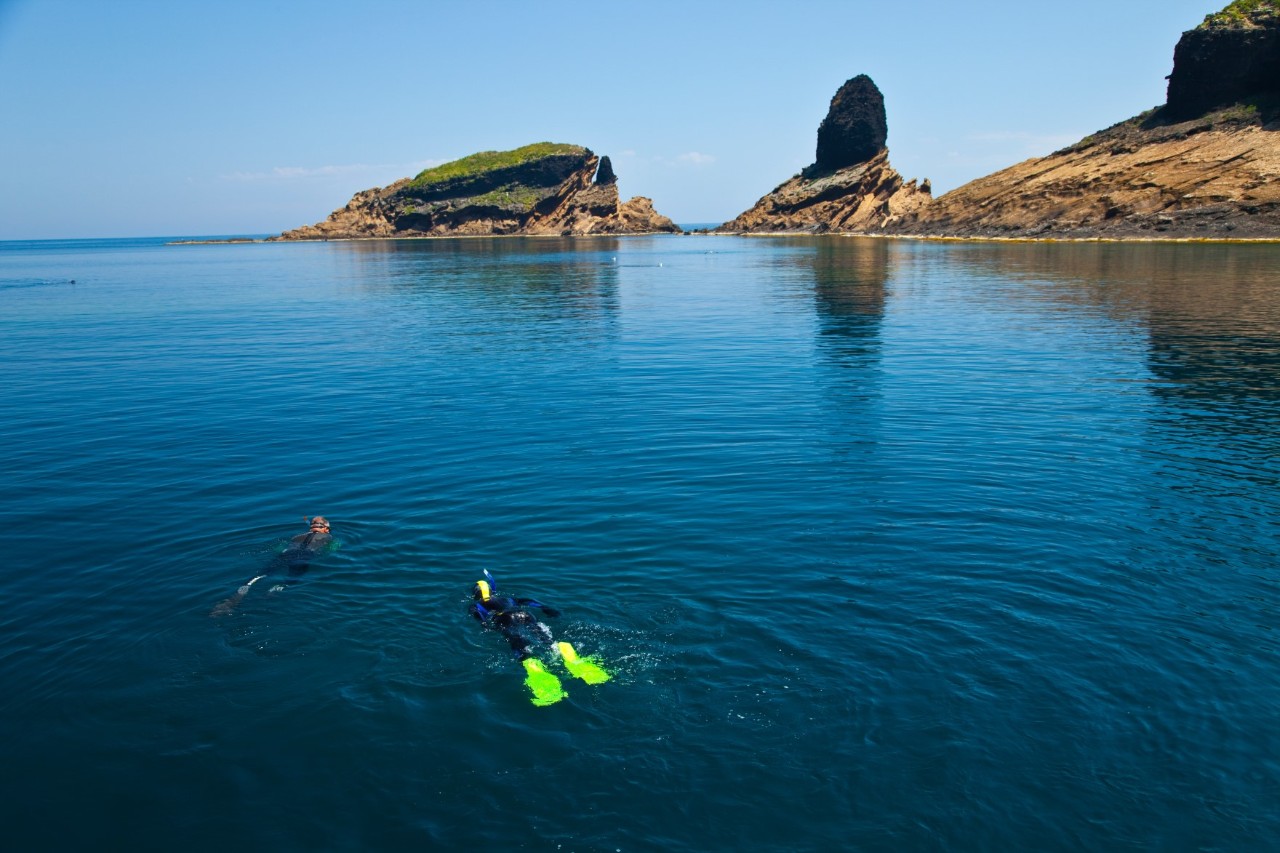 Zwei Menschen, die an der Meeresoberfläche schnorcheln, im Hintergrund karge Inselberge © Juan Carlos Munoz/stock.adobe.com 