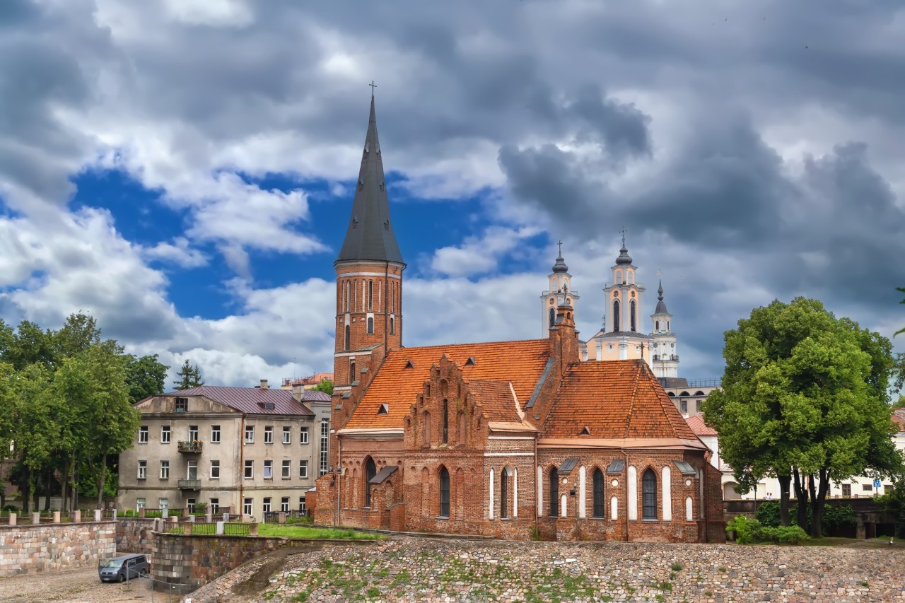 Rote Kirche mit spitzem Turm, umgeben von Bäumen. Im Hintergrund weitere Kirchtürme und Häuser © borisb17/stock.adobe.com 